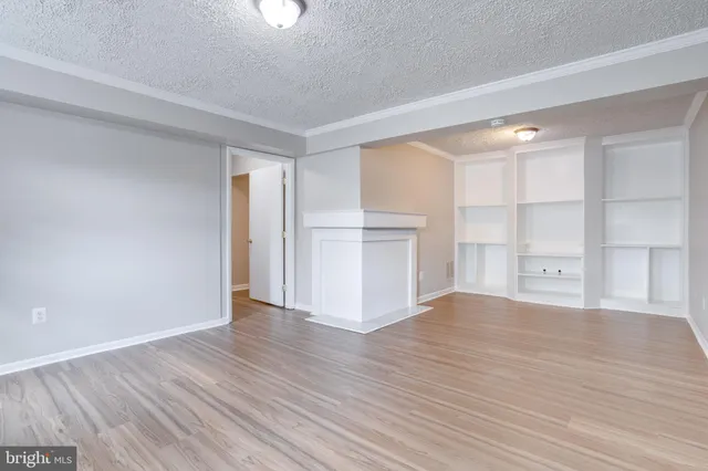 a view of empty room with wooden floor and kitchen