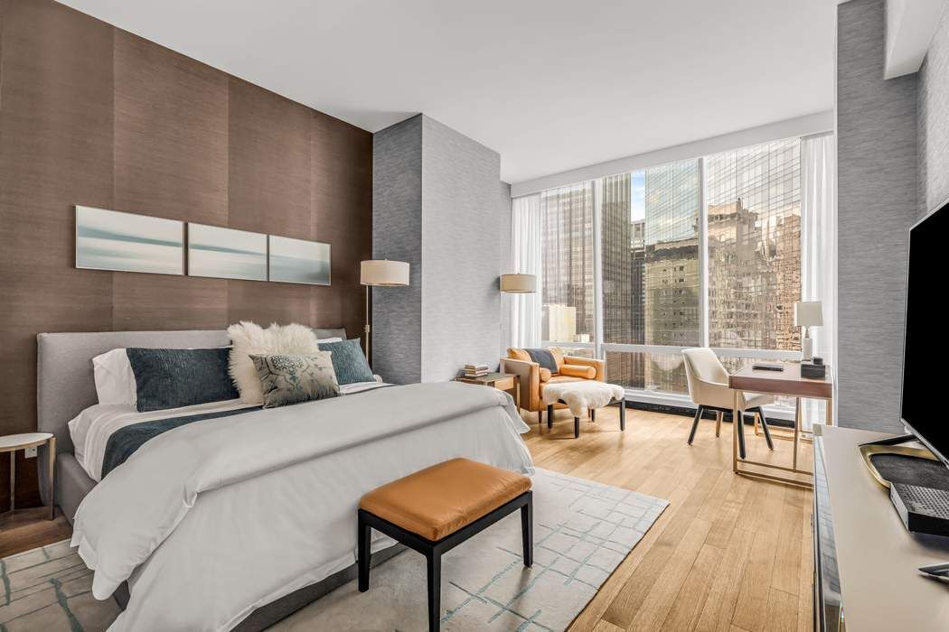 157 West 57th Street, Unit 35E Manhattan, NY 10019 - Photo 6 of 12 a bedroom with a bed a large window and wooden floor