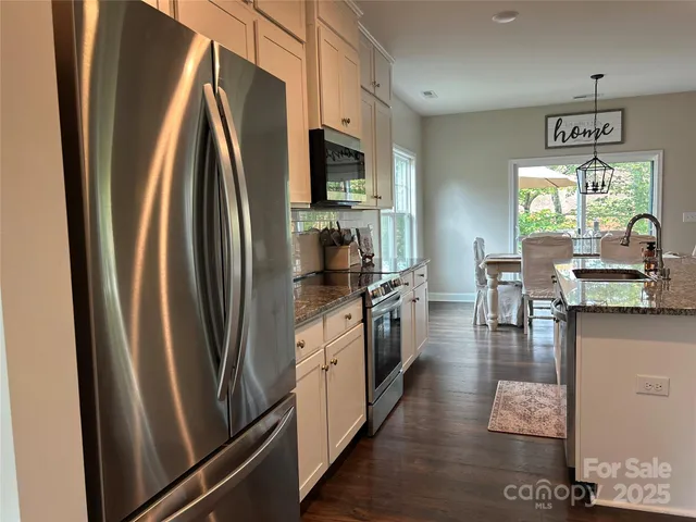 a living room with stainless steel appliances kitchen island granite countertop a table chairs and a view of living room