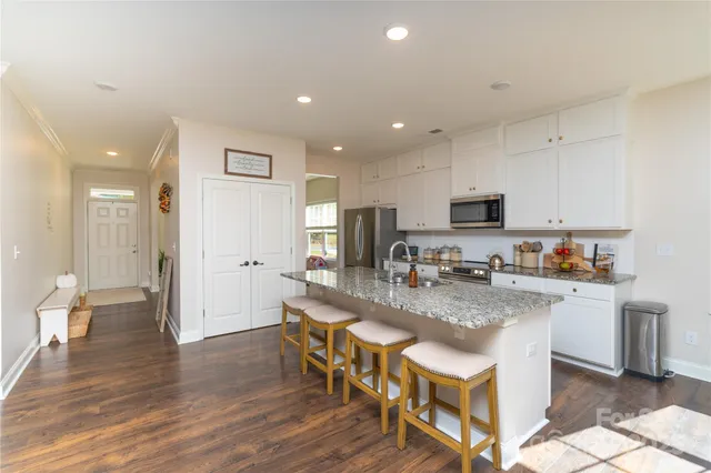 a kitchen with stainless steel appliances granite countertop a dining table chairs refrigerator and microwave