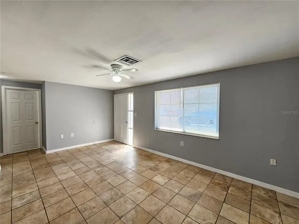 a view of an empty room with window and chandelier fan