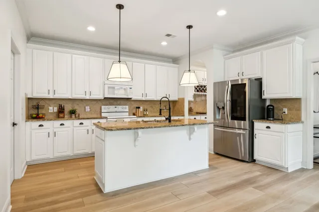 a kitchen with stainless steel appliances granite countertop a refrigerator a sink dishwasher a stove and white cabinets with wooden floor