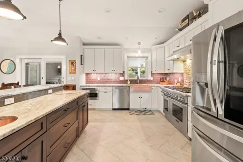 a kitchen with stainless steel appliances granite countertop a sink a stove a refrigerator cabinets and a window