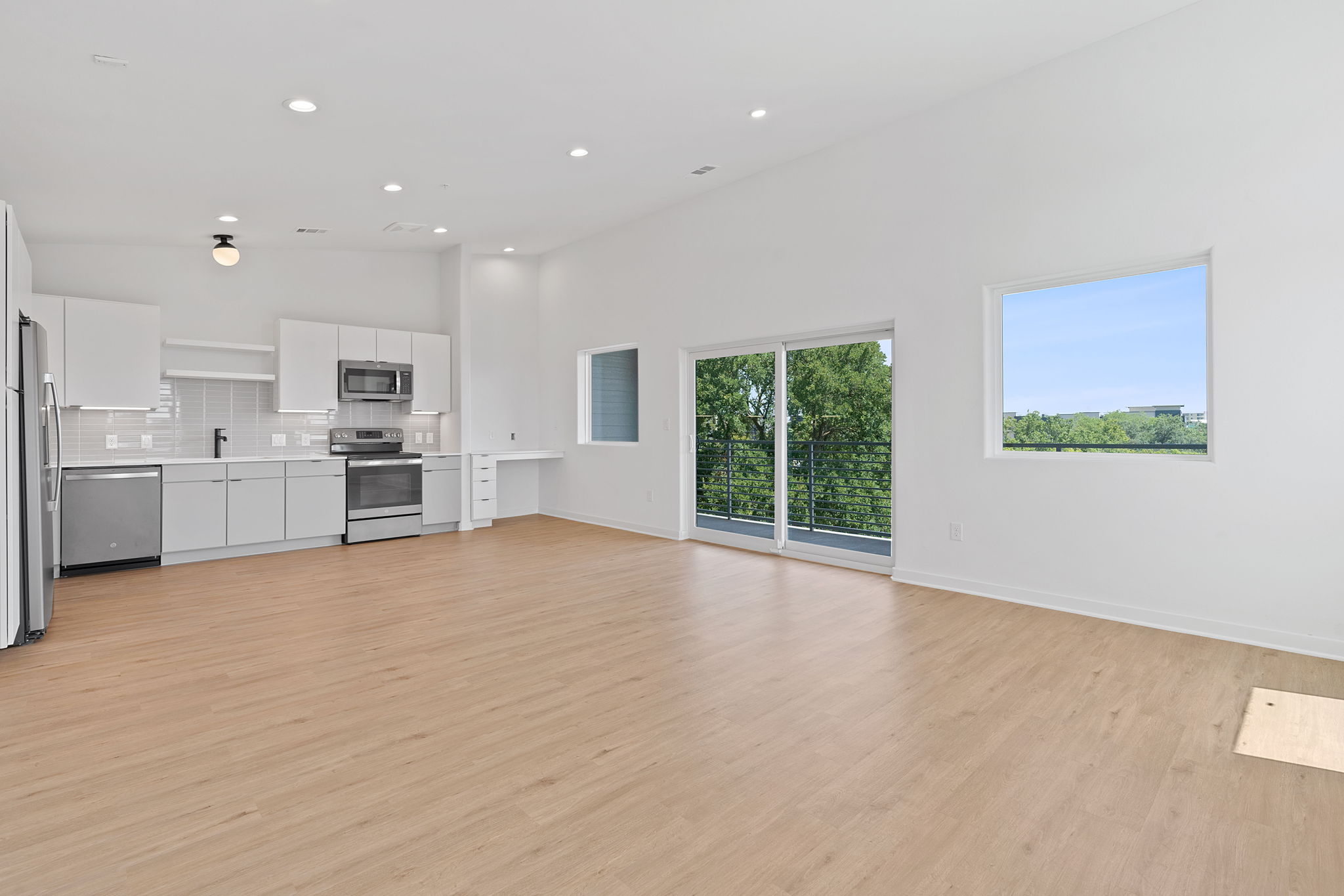 Unfurnished living room featuring a high ceiling, light wood-style flooring, and recessed lighting