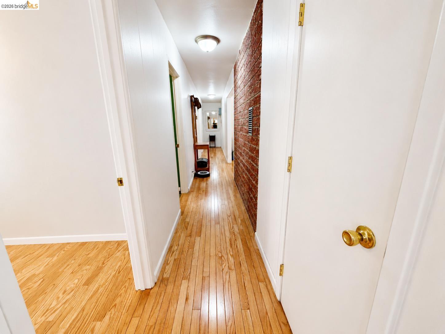 18195 Wards Ferry Road Sonora, CA 95370 - Photo 26 of 67 Hallway featuring wood-finish flooring, exposed brick accent wall, white painted walls, and overhead lighting fixtures