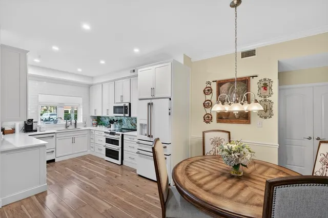 a kitchen with stainless steel appliances granite countertop a sink dishwasher a refrigerator and white cabinets with wooden floor