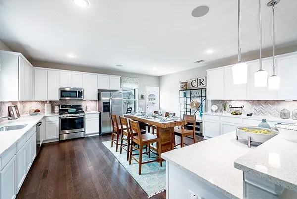 a open kitchen with stainless steel appliances kitchen island granite countertop a stove top oven a sink a dining table and chairs with wooden floor