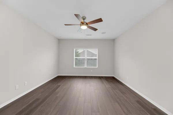an empty room with wooden floor ceiling fan and windows