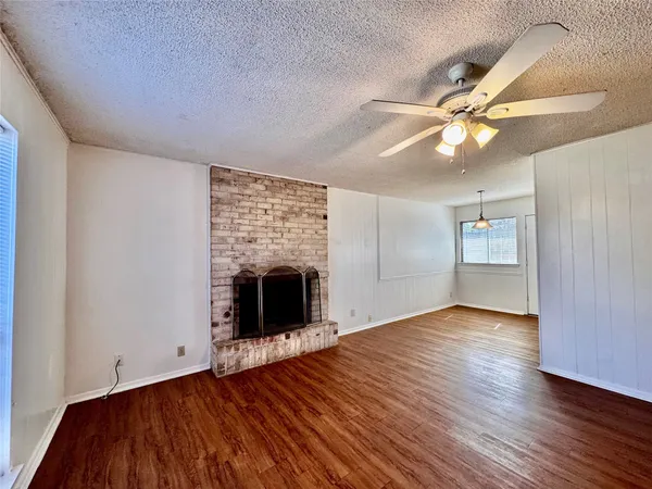 an empty room with wooden floor a ceiling fan and fireplace