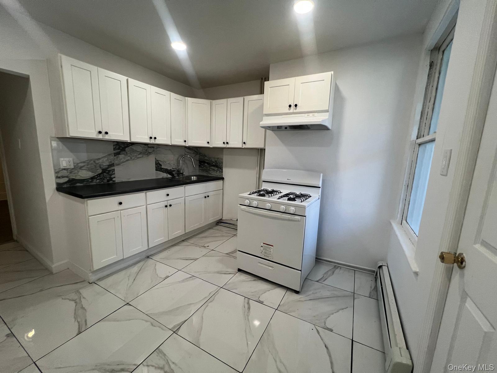 Kitchen featuring dark countertops, gas range gas stove, baseboard heating, white cabinets, and light marble finish flooring
