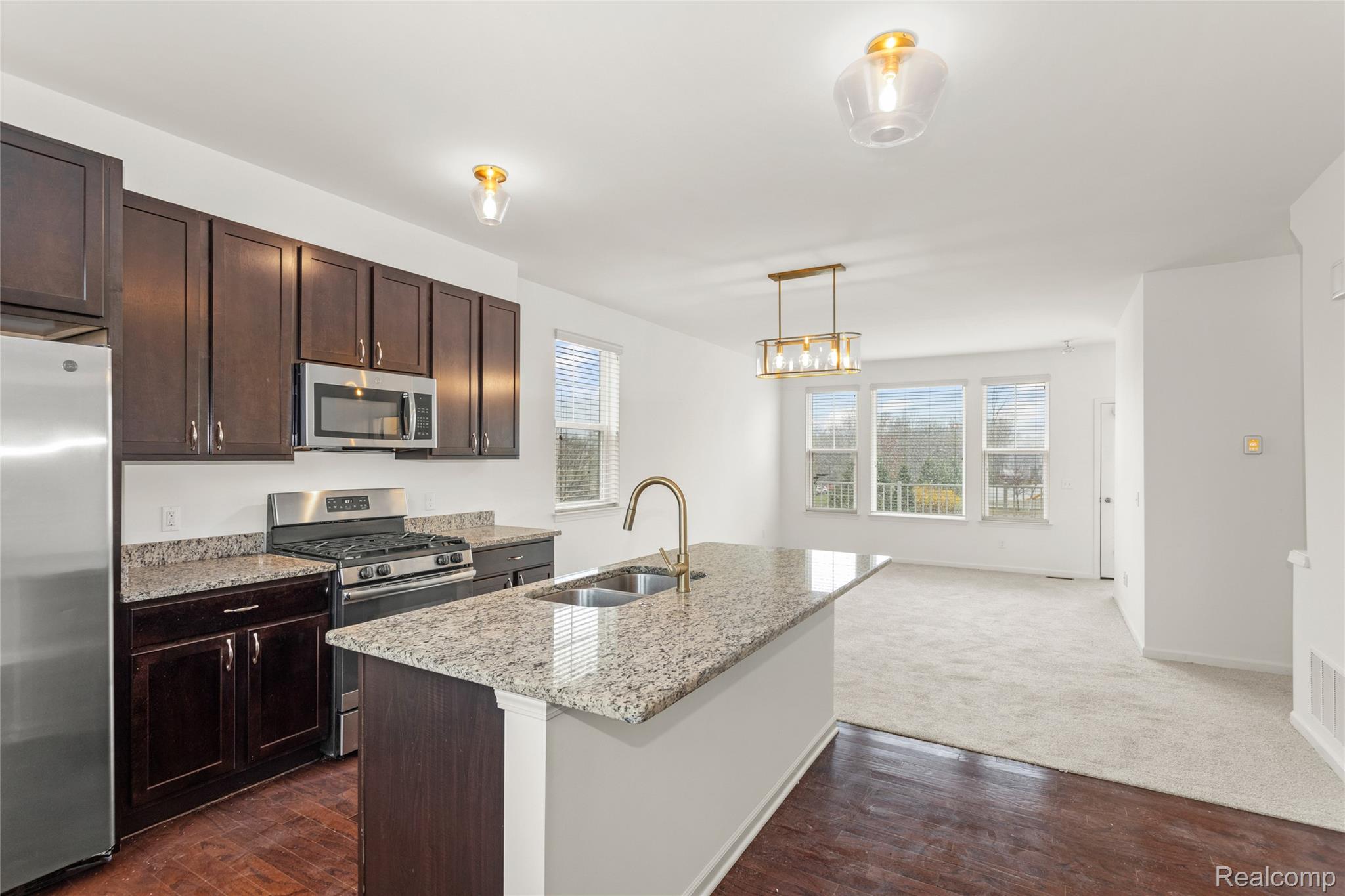 478 North Wixom Road Wixom, MI 48393 - Photo 7 of 26 Kitchen featuring stainless steel appliances, dark wood finish cabinets, light stone counters, and a kitchen island with sink