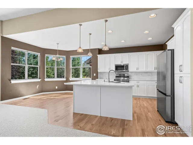 a open kitchen with stainless steel appliances granite countertop a refrigerator a sink dishwasher a stove and white cabinets with wooden floor