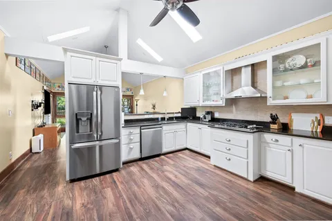 a kitchen with granite countertop a refrigerator oven a sink dishwasher and white cabinets with wooden floor