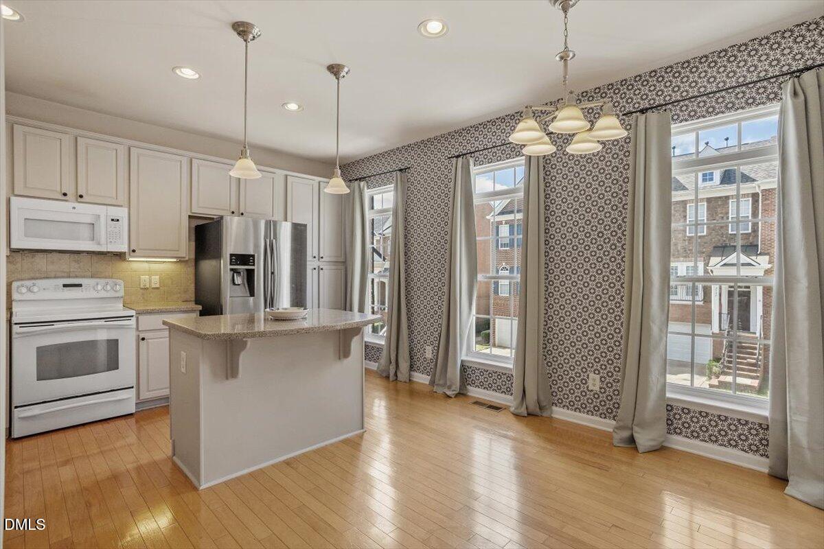 a kitchen with stainless steel appliances kitchen island granite countertop a refrigerator a stove and white cabinets with wooden floor