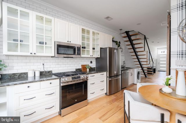 a kitchen with stainless steel appliances granite countertop a stove top oven a sink dishwasher a refrigerator and a dining table with wooden floor