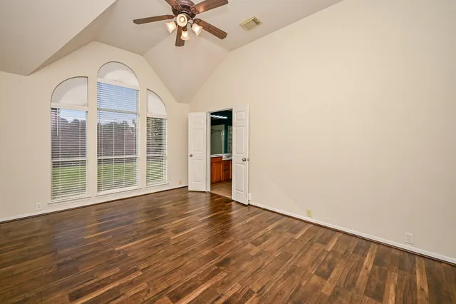 an empty room with wooden floor fan and windows