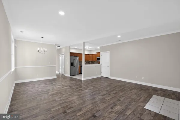 a view of an empty room with wooden floor kitchen view and a window