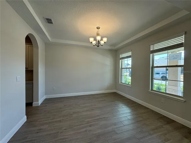 an empty room with wooden floor chandelier and windows