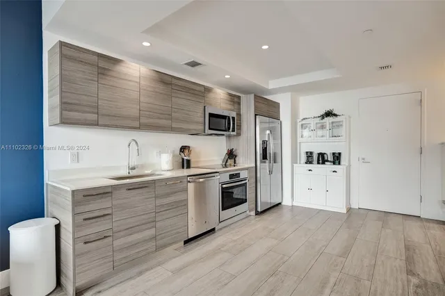 a kitchen with stainless steel appliances a stove top oven a sink a refrigerator white cabinets and wooden floor