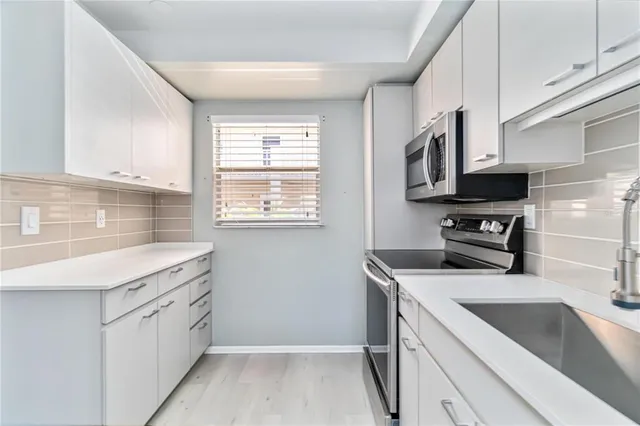 a kitchen with stainless steel appliances a sink a stove a microwave and white cabinets