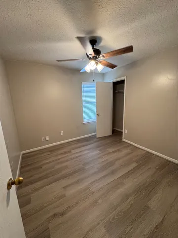 a view of an empty room with wooden floor and a ceiling fan