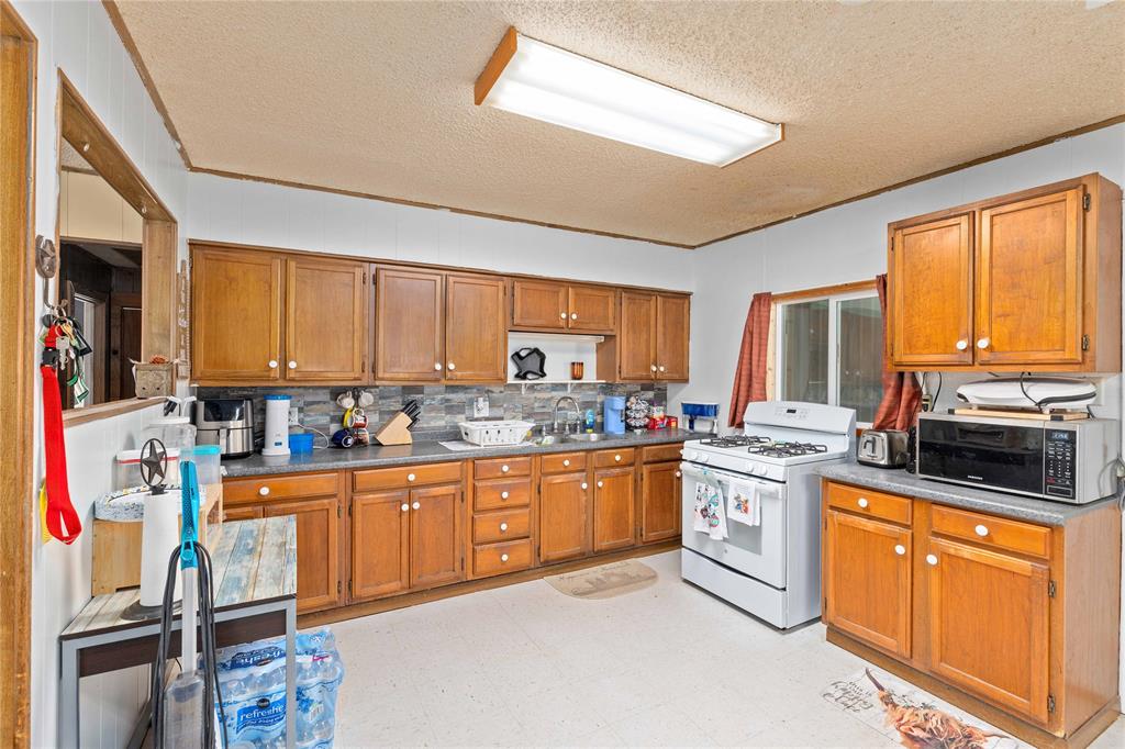 309 Goodwin Street Bangs, TX 76823 - Photo 8 of 20 Kitchen featuring brown cabinets, light flooring, white gas range, dark countertops, and a textured ceiling