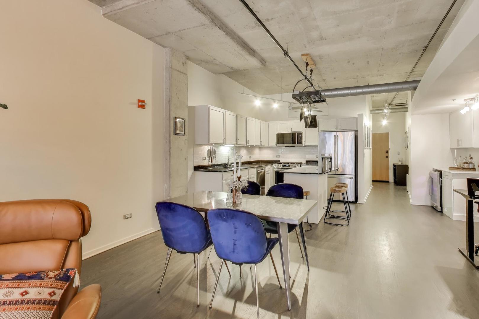 933 West Van Buren Street, Unit 504 Chicago, IL 60607 - Photo 9 of 31 a kitchen with stainless steel appliances kitchen island granite countertop a refrigerator a stove a microwave oven a dining table and chairs with wooden floor