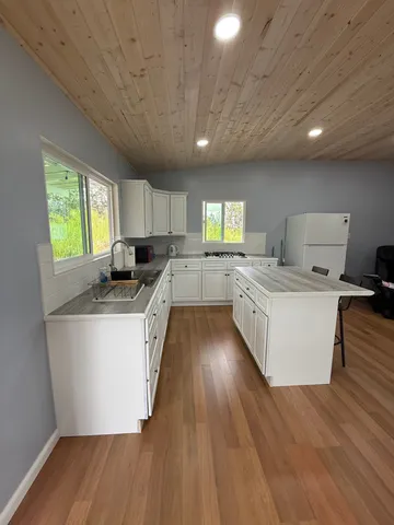 a large kitchen with stainless steel appliances granite countertop a stove a sink dishwasher a microwave oven and a large island with wooden floor