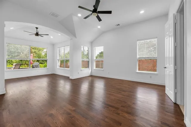 an empty room with wooden floor windows and ceiling fan