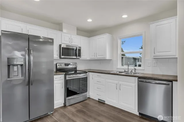 a kitchen with stainless steel appliances granite countertop a refrigerator a stove a sink and white cabinets