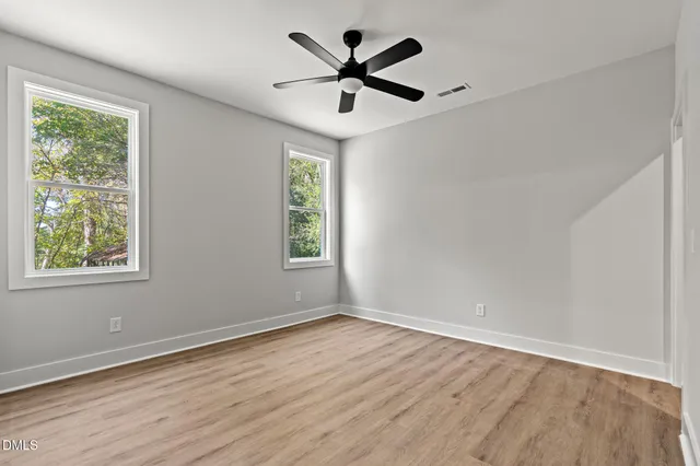 an empty room with wooden floor fan and windows