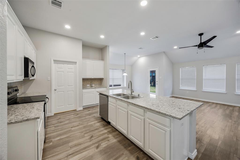 3603 Cottonwood Road Melissa, TX 75454 - Photo 5 of 27 Kitchen featuring white cabinetry, stainless steel appliances, light wood-style floors, light stone countertops, and a kitchen island with sink