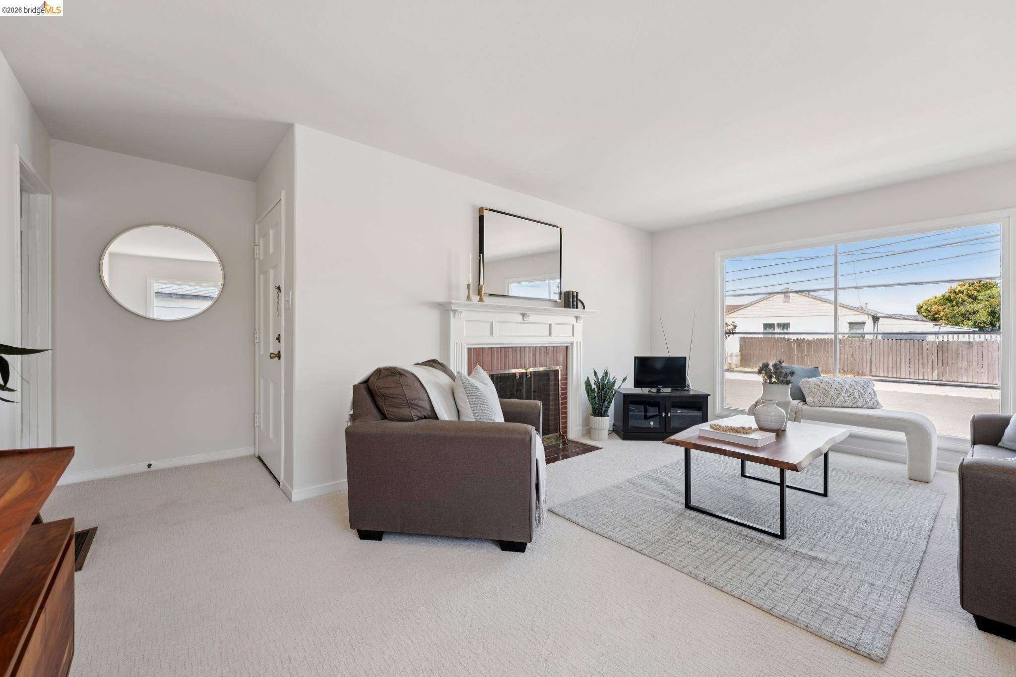 15162 Inverness Street San Leandro, CA 94579 - Photo 6 of 25 Bright living area featuring a prominent window, a detailed fireplace with a white mantel, and neutral-toned carpeting throughout