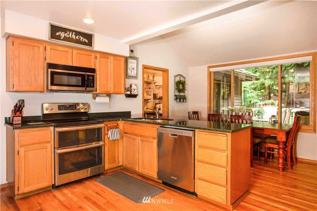 3205 211th Street Southeast Bothell, WA 98021 - Photo 14 of 40 a kitchen with stainless steel appliances granite countertop a stove top oven a sink dishwasher a dining table and chairs with wooden floor