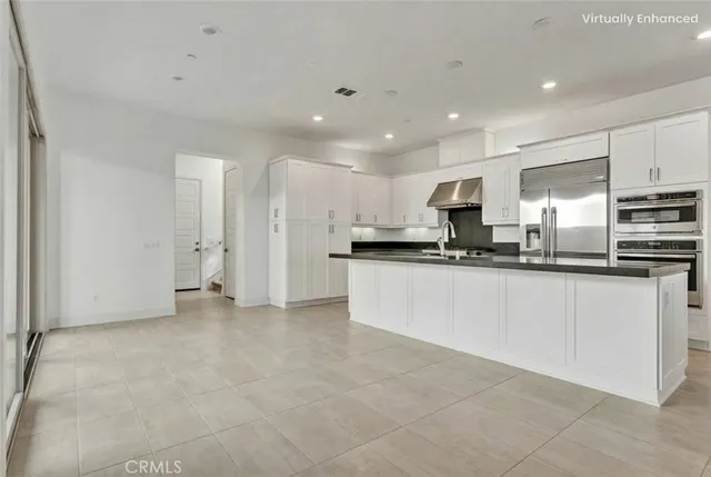 a large white kitchen with kitchen island a sink a center island stainless steel appliances and a refrigerator