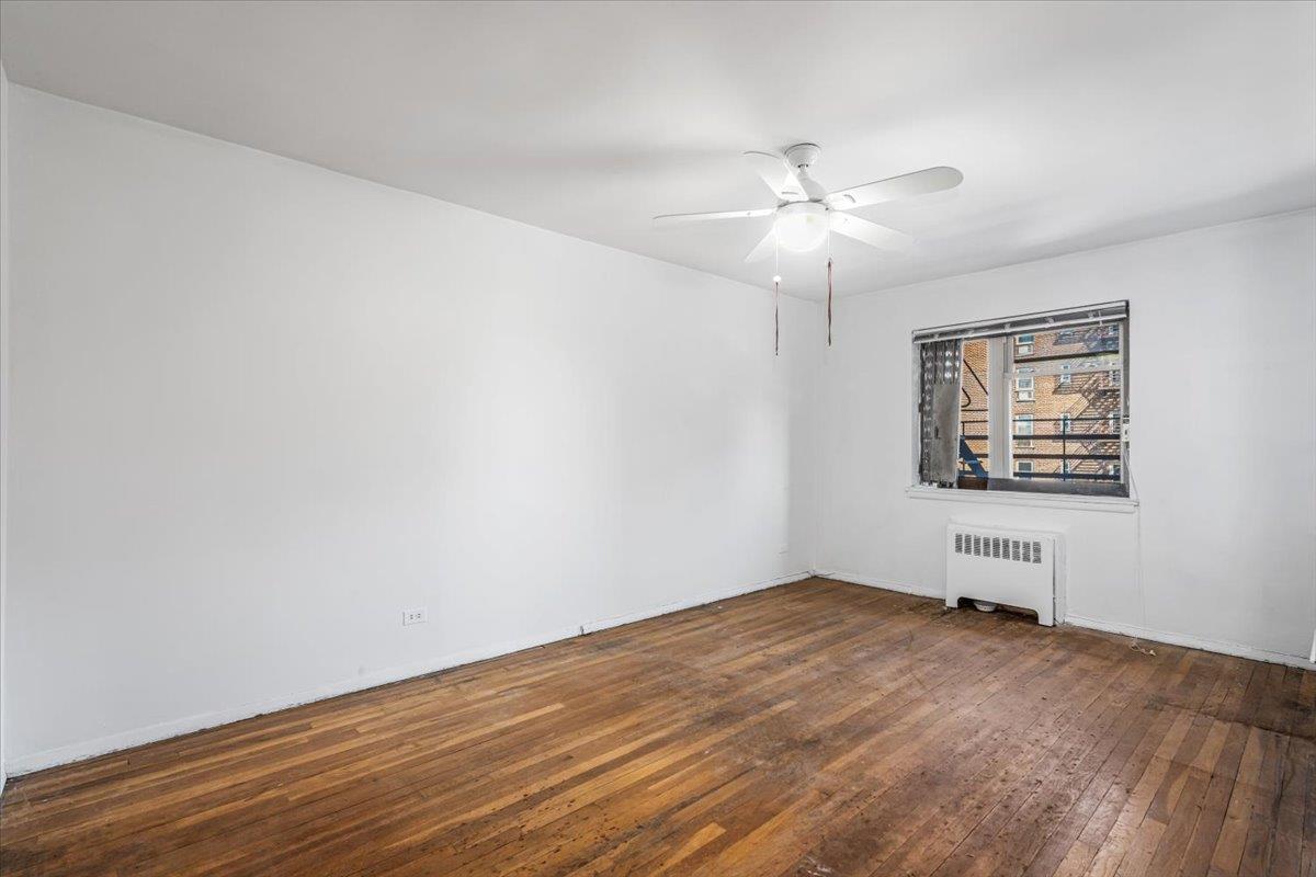 144-55 Melbourne Avenue, Unit 3J Queens, NY 11367 - Photo 9 of 13 Empty room featuring wood-type flooring, a ceiling fan, radiator, and baseboards