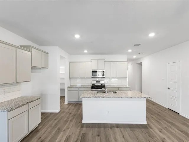 a view of kitchen with granite countertop a stove top oven a sink a refrigerator and white cabinets with wooden floor