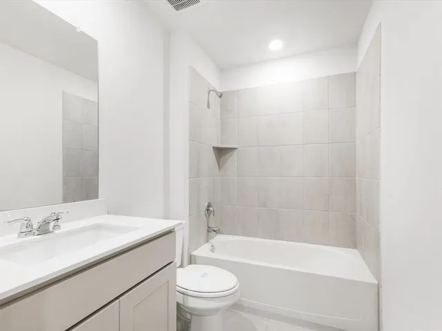 a bathroom with a granite countertop bathtub shower sink vanity mirror and toilet