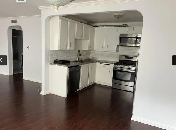 an empty room with wooden floor and a kitchen