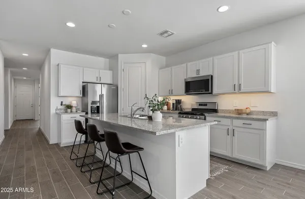a kitchen with stainless steel appliances a stove a sink a refrigerator white cabinets and a chairs