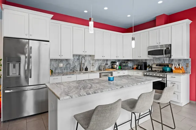 a kitchen with kitchen island granite countertop a stove a sink a refrigerator and white cabinets