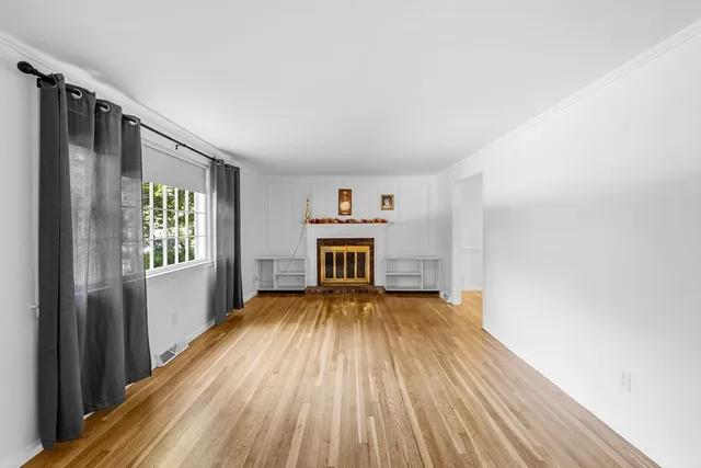 a view of an empty room with wooden floor fireplace and a window
