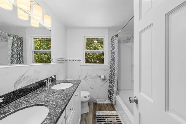 a bathroom with a granite countertop sink a mirror a toilet and a shower