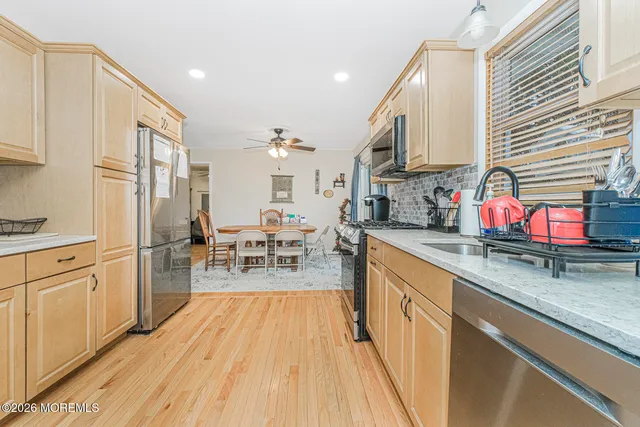 a kitchen with stainless steel appliances granite countertop a refrigerator a sink dishwasher a stove and white countertops with wooden floor