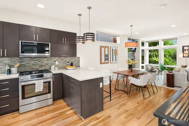 a kitchen with stainless steel appliances granite countertop a stove a refrigerator a microwave a dining table and chairs with wooden floor