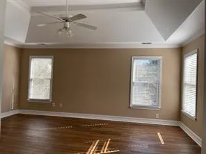 an empty room with wooden floor chandelier fan and windows