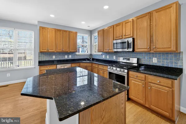 a kitchen with granite countertop cabinets stainless steel appliances wooden floor and a window