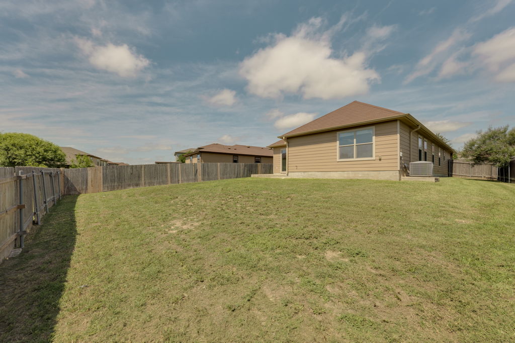 210 Cushman Drive Kyle, TX 78640 - Photo 20 of 21 Expansive backyard featuring a sloped lawn, full privacy fencing, and a tan siding exterior with multiple windows