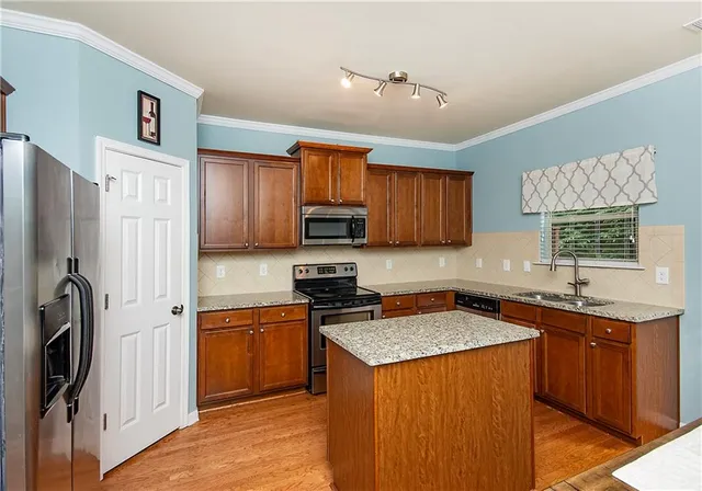 a kitchen with stainless steel appliances granite countertop a stove top oven a refrigerator a sink and dishwasher with wooden cabinets