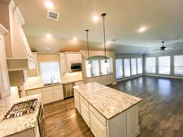 a kitchen with stainless steel appliances granite countertop wooden cabinets a sink dishwasher and a stove with wooden floor